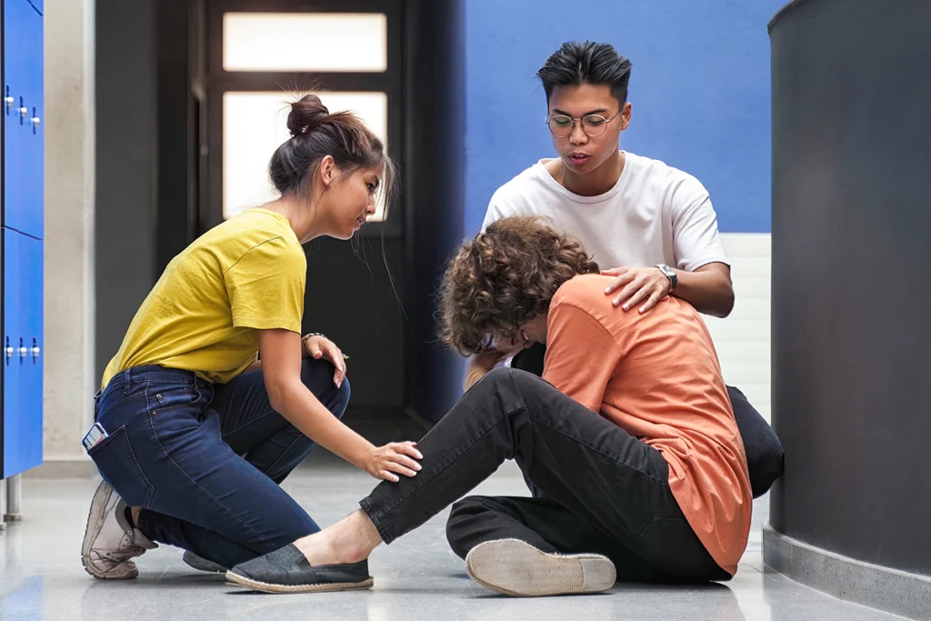Two students comforting their classmate sitting on the floor in college hallway.